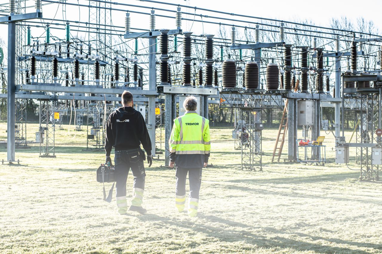 gallery-04 Two workers inspect an outdoor electrical substation, emphasizing safety and maintenance.