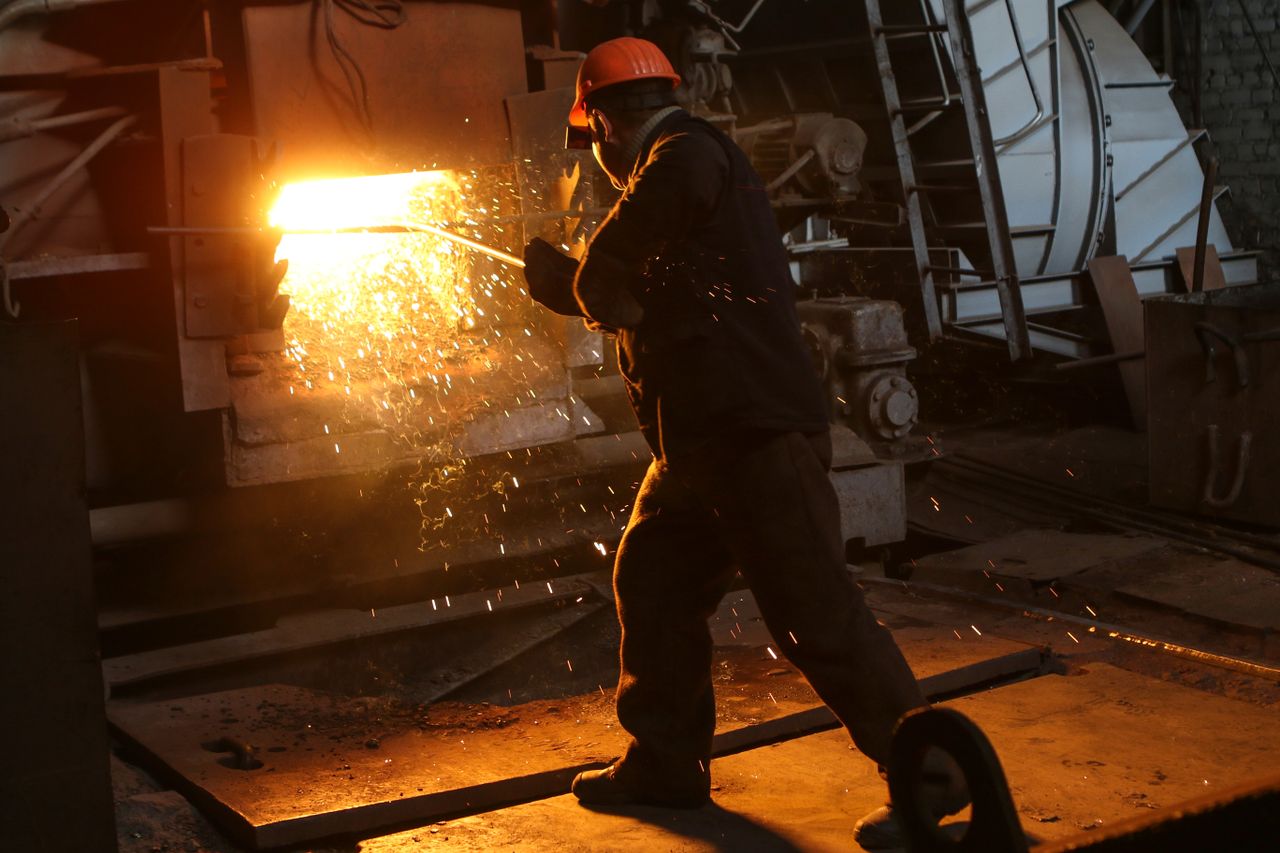 gallery-03 A worker in protective gear welds metal in an industrial plant with sparks flying.